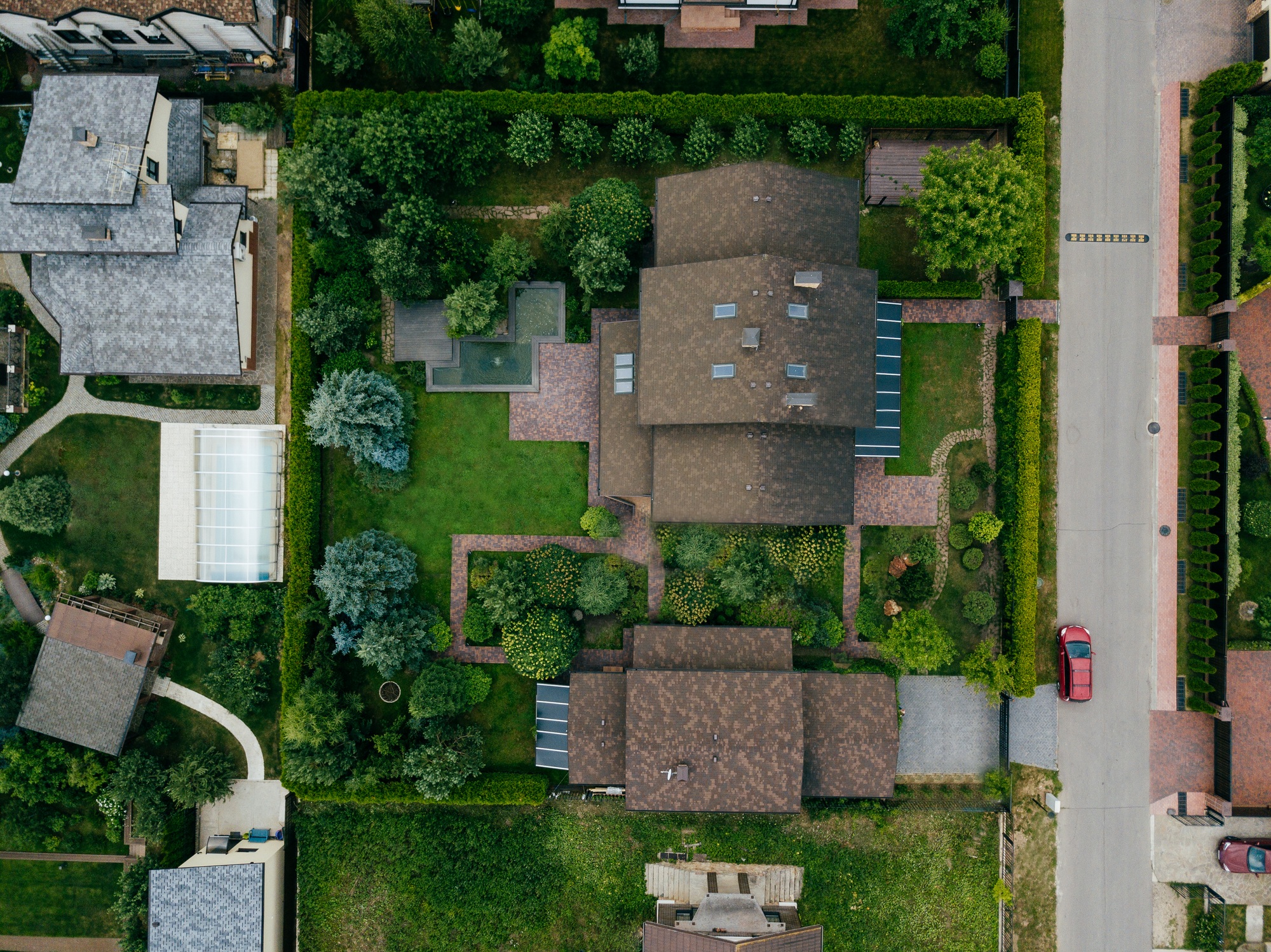 Aerial top view of house shingle roof and car on paved yard with green grass lawn.